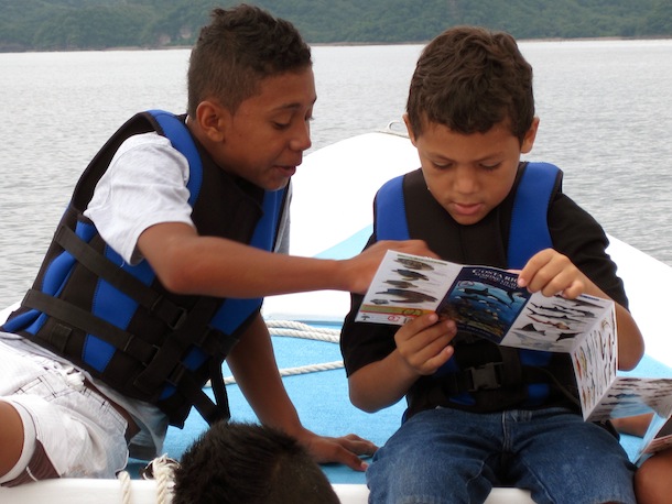 2 boys in a boat intently looking at a field guide